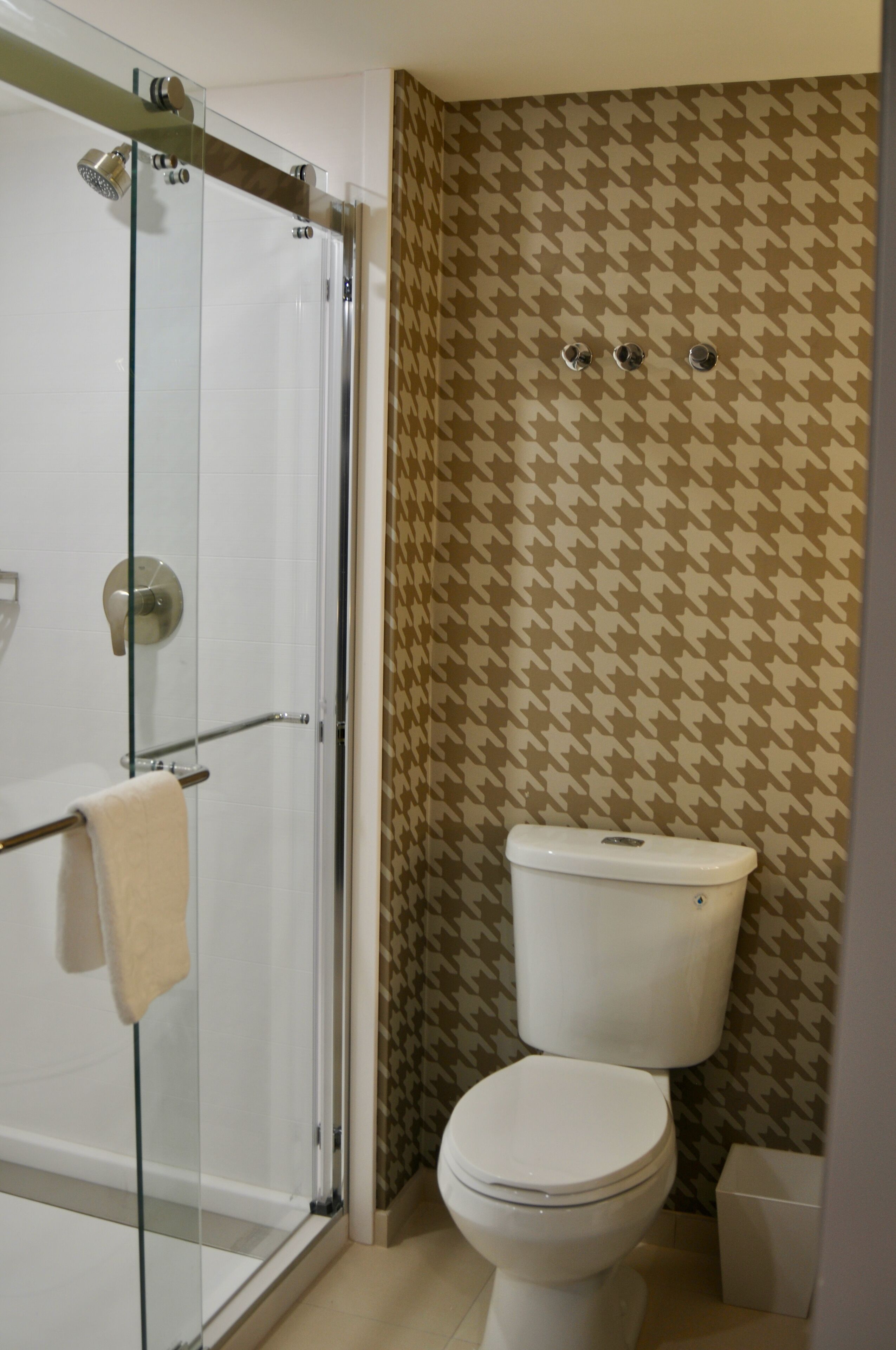 Een badkamer met een douchecabine van glas, een toilet en behang met een patroon.