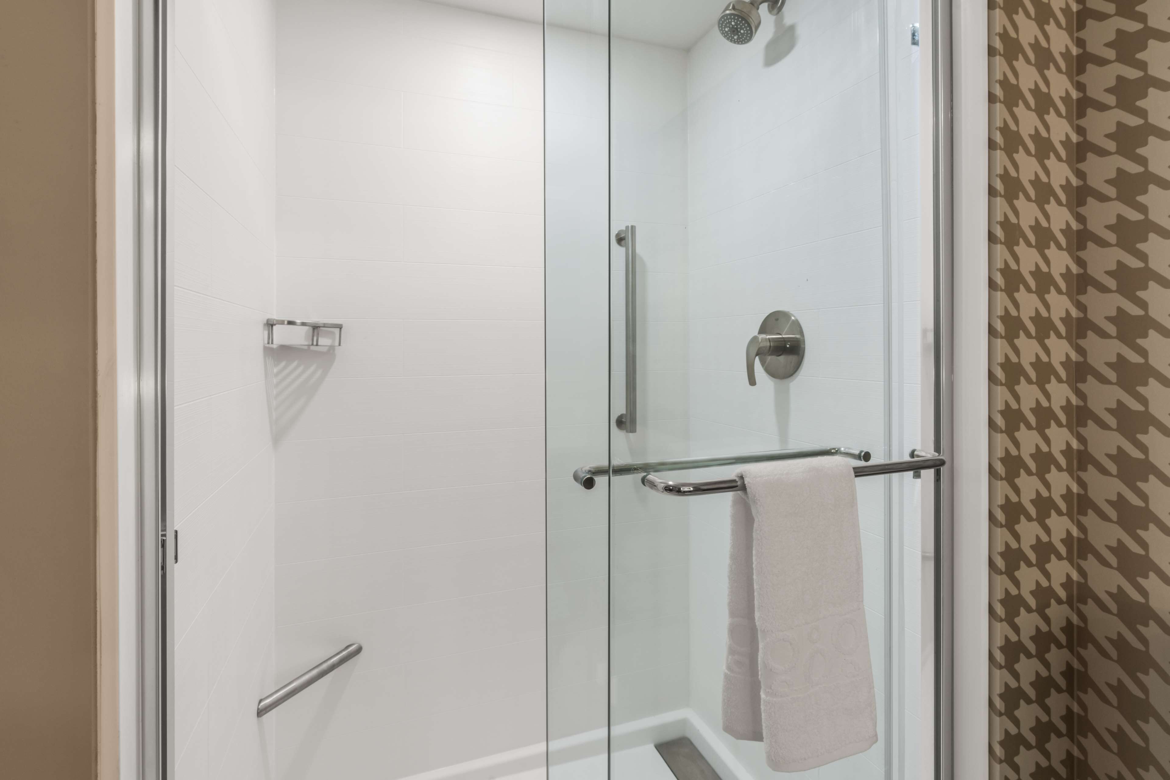 A glass-enclosed shower with a towel rack and a handheld showerhead.