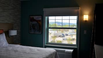 Quarto de hotel com cama, janela com vista para o exterior, luminária na parede e um quadro.