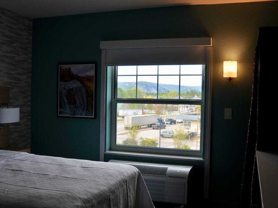 Quarto de hotel com cama, janela com vista para o exterior, luminária na parede e um quadro.