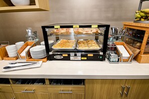 A buffet setup with trays of food, utensils, and condiments. - Home2 Suites by Hilton North Conway (North Conway)