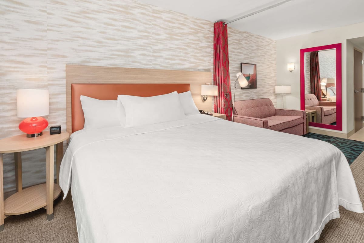 A hotel room with a large bed, a desk with a lamp, a chair, and a mirror.