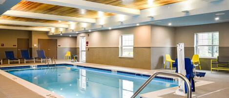 Una piscina interior con marcas claras de carril, techo de madera y varias sillas de descanso.