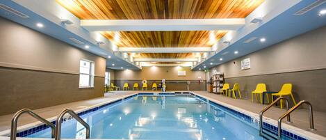 An indoor swimming pool with wooden ceiling, tiled floor, and yellow chairs along the side.
