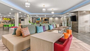 A modern lounge area with a sofa, a wooden table, and red chairs. - Home2 Suites by Hilton North Conway (North Conway)