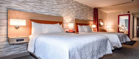 A hotel room with two beds, each with a wooden headboard, bedside lamps, and a nightstand.