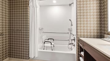 Un baño moderno con ducha a nivel de suelo, una bañera blanca con barandilla de seguridad y un lavamanos con espejo.