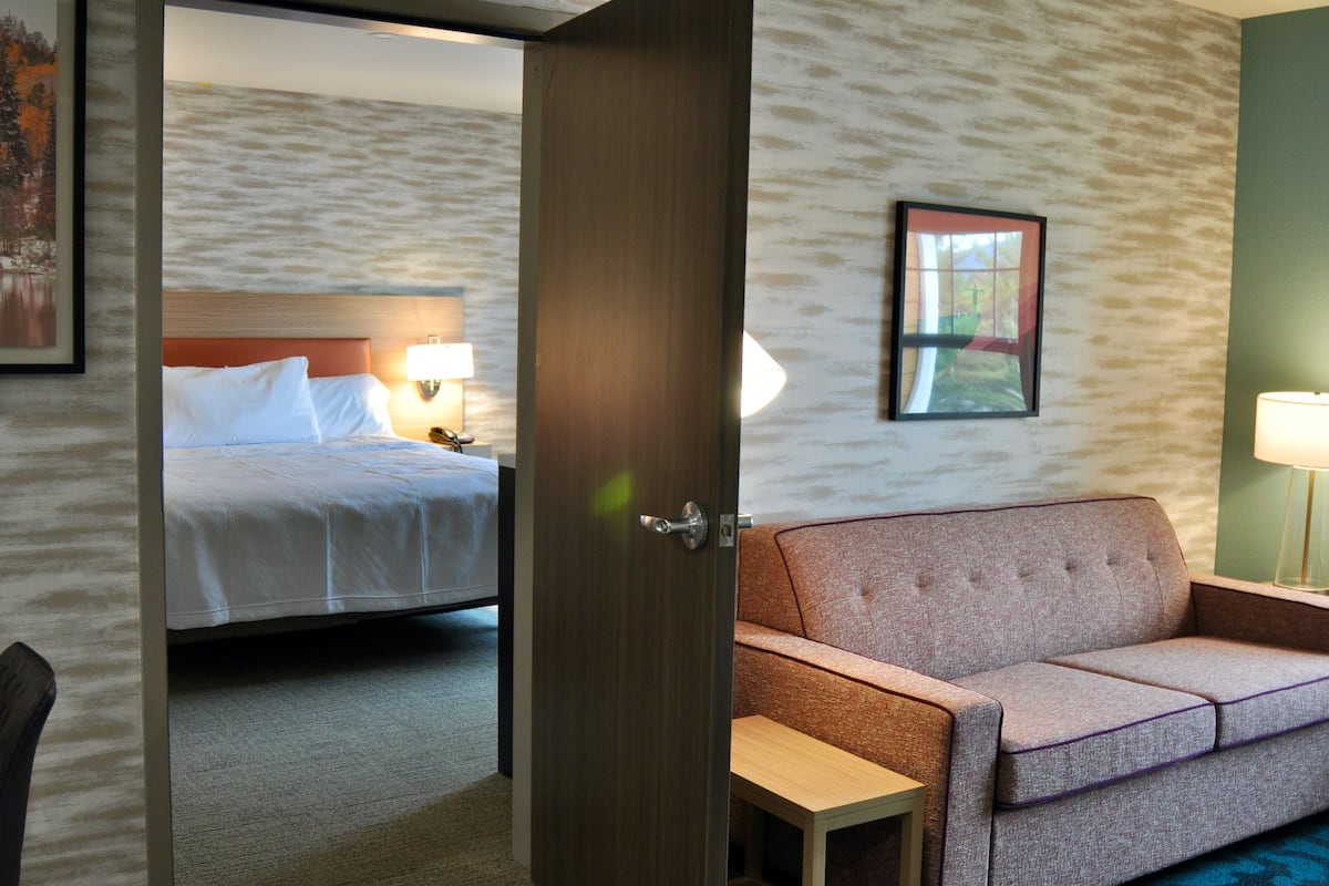 A hotel room with a bed, a sofa, a small table, and a door leading to another room.