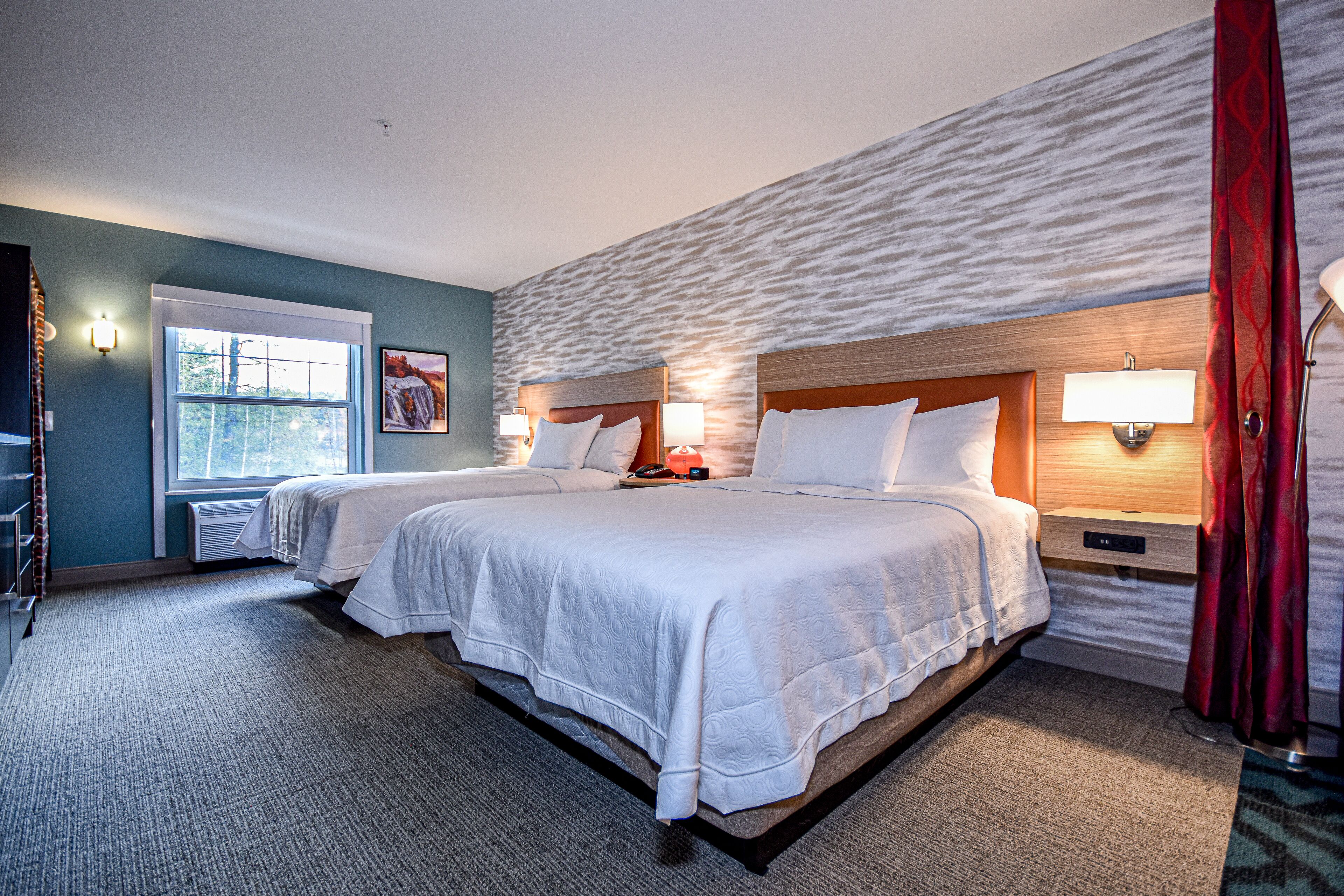 A hotel room with two beds, a large window, and a stone-textured wall.