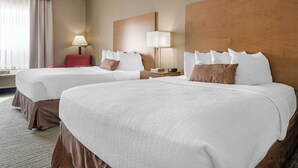 A hotel room with two beds, a red chair, two bedside tables with lamps, and a large window with curtains. - Best Western Plus Jefferson (Jefferson)