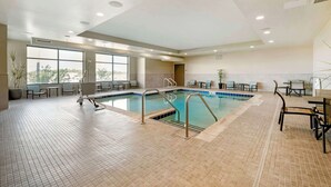 An indoor swimming pool with tiled flooring, metal pool ladders, and seating areas with tables and chairs. - Best Western Plus Jefferson (Jefferson)
