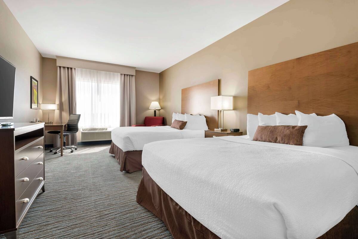 A hotel room with two beds, a desk, a chair, and a TV.