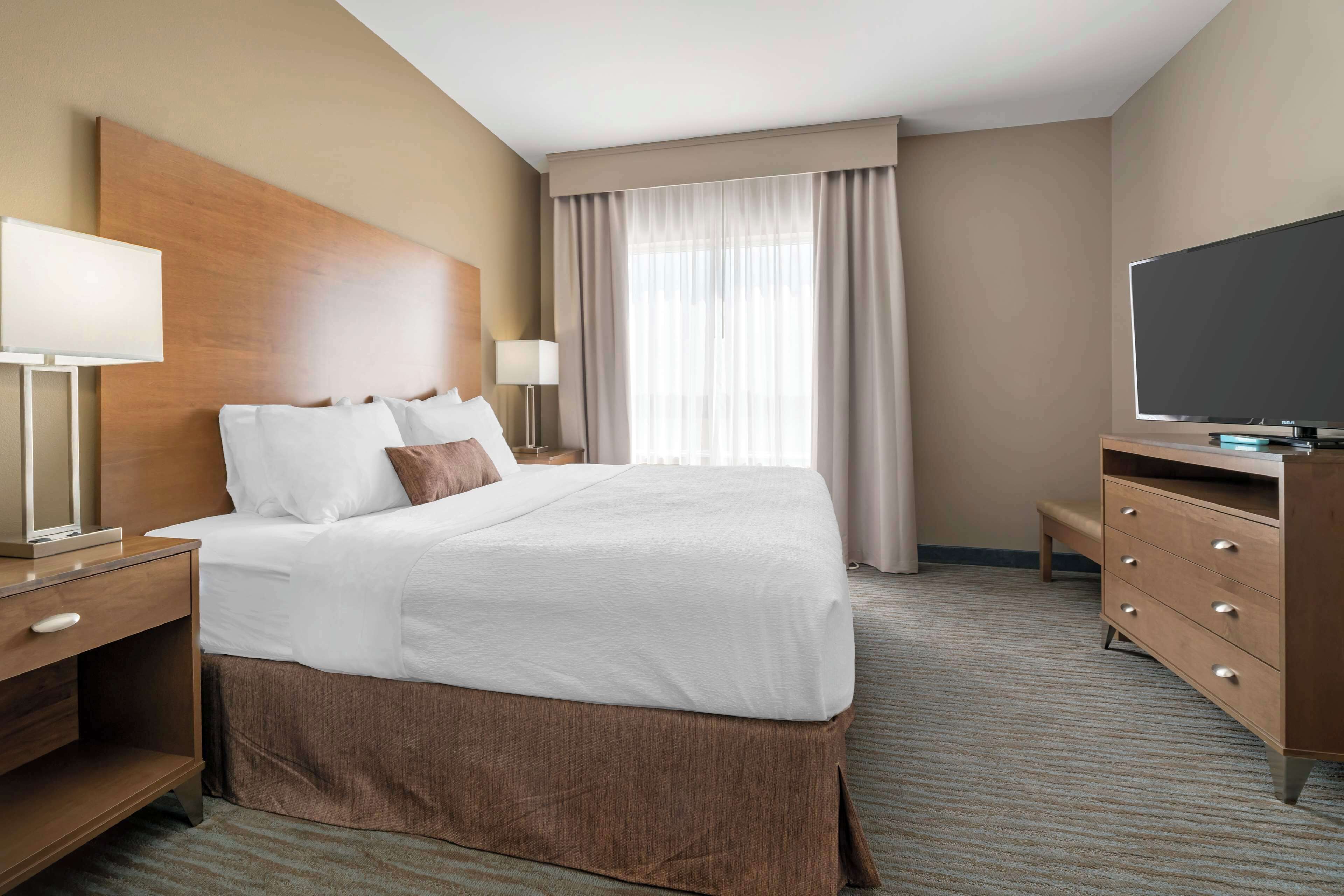 A hotel room with a large bed, bedside tables, a TV, and a window with curtains.
