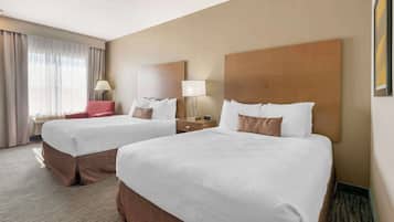 A hotel room with two beds, a desk, a chair, and a large window with curtains.