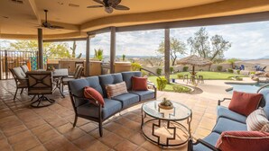 A covered patio with a blue sofa, a glass coffee table, and a dining area with chairs and a table. - Happy Valley Hideaway | Resort-like home with amazing views & walking distance to hiking trails! (Phoenix)