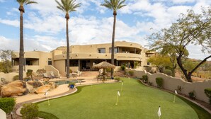 A golf course with a pool, palm trees, and a large building with multiple windows and balconies. - Happy Valley Hideaway | Resort-like home with amazing views & walking distance to hiking trails! (Phoenix)