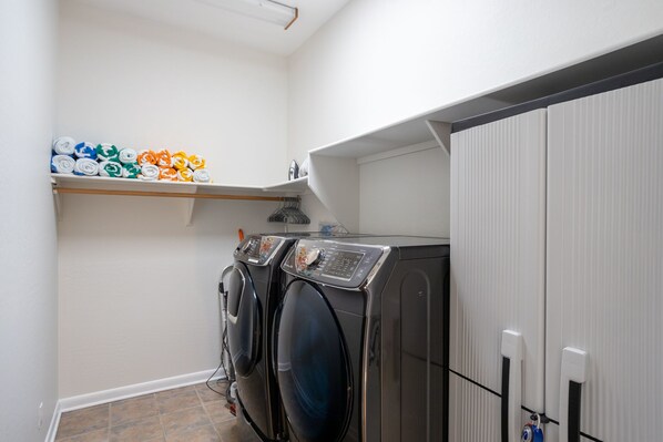 A laundry area with two front-loading washers and dryers, a shelf with folded towels, and a white wall.