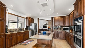 A spacious kitchen with wooden cabinets, granite countertops, a central island, and stainless steel appliances. - Happy Valley Hideaway | Resort-like home with amazing views & walking distance to hiking trails! (Phoenix)