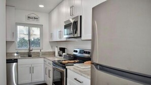 Una cocina moderna con armarios blancos, electrodomésticos de acero inoxidable y un ventanal con persianas.