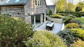 A rustic wooden house with a sloped roof, large windows, and a patio with outdoor furniture.