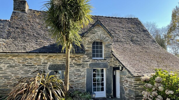 A stone house with a tiled roof, a central window, and a door.