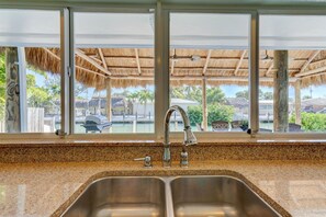 Cocina con encimera de granito, pileta de acero inoxidable y vista a un área de piscina con techos de paja.