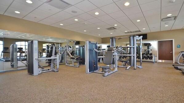 A gym with various exercise machines, a mirrored wall, and a carpeted floor.
