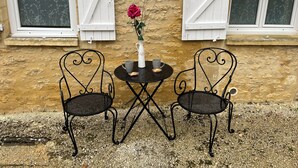 A rustic outdoor seating area with two metal chairs and a small round table, set against a textured stone wall with white shutters. - Rent Sarlat in Perigord  (Sarlat-la-Canéda)