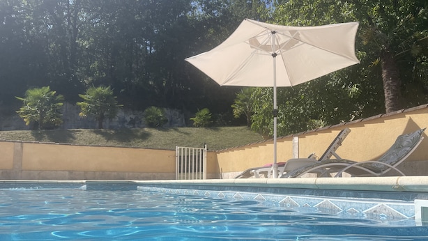 A swimming pool with clear blue water, surrounded by a low wall and a gate. There are lounge chairs and a large umbrella providing shade. - Rent Sarlat in Perigord  (Sarlat-la-Canéda)