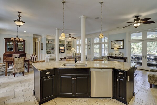 A spacious kitchen with a large island, dark cabinetry, and a modern faucet. There are pendant lights, a ceiling fan, and a view of the outdoors through large windows. - 1 Roadrunner - 4th Row (45-yard walk) to the Ocean, Private Pool & Spa (Hilton Head Island)