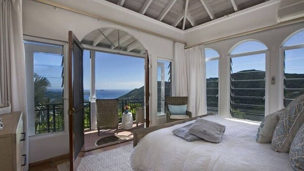 Ein Schlafzimmer mit einem großen Bett, Meerblick und einem Balkon mit Korbmöbeln.