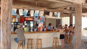 Zona de bar con taburetes de madera, una barra y cajas de cerveza Corona colgadas.