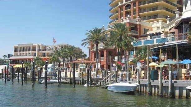 Una zona ribereña con muelle, un barco y edificios con balcones.