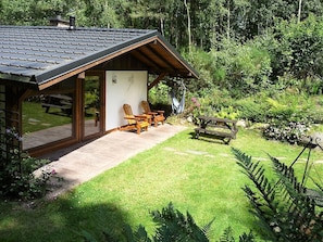 Une cabane dotée d’un patio couvert, de chaises en bois et d’un hamac.