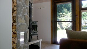 Un mur en pierre avec un poêle à bois, un banc blanc et une vue sur un jardin, visible à travers une porte vitrée.
