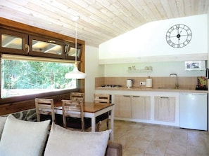Une cuisine chaleureuse avec des meubles en bois, une table à manger avec des chaises, une horloge et une fenêtre donnant sur un espace verdoyant.