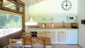 Une cuisine avec des meubles de rangement en bois, une table à manger avec des chaises, un luminaire suspendu, une horloge murale, un four à micro-ondes et un évier.
