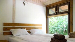 Un lit double avec du linge de lit blanc, une tête de lit en bois et une fenêtre donnant sur un paysage verdoyant.