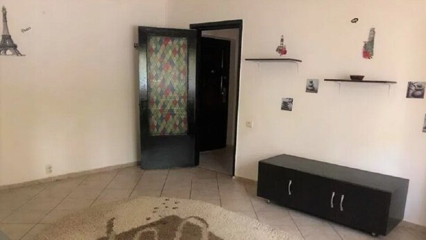 Una habitación con un tapete estampado, un mueble negro y una puerta que da a otra estancia.