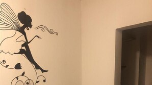 Un rincón de una habitación con un adhesivo de pared de una hada, un estante empotrado y una lavadora en la habitación contigua.