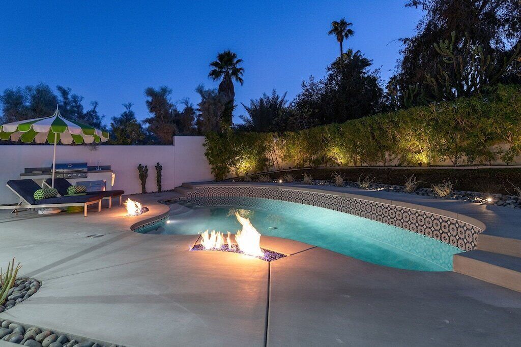 A swimming pool with a fire feature, lounge chairs, and a decorative umbrella.