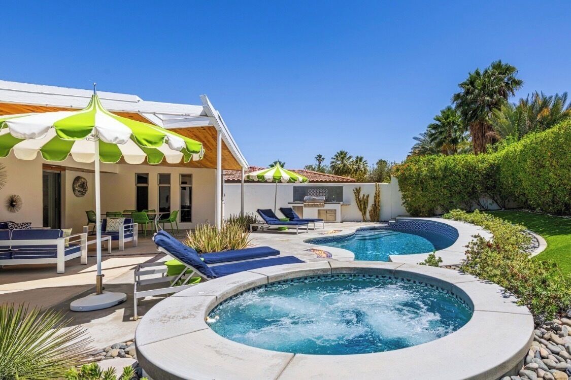 A pool area with lounge chairs, a hot tub, and a covered seating area.
