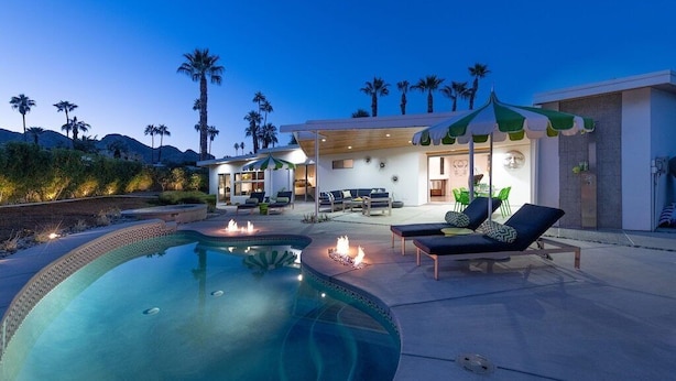 A modern outdoor pool area with lounge chairs, a fire pit, and a covered seating area. - An Extra Hour of Sunshine, Southern California Desert (Rancho Mirage)