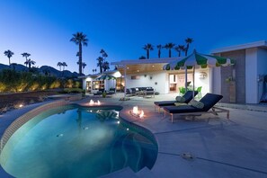 A modern outdoor pool area with lounge chairs, a fire pit, and a covered seating area.