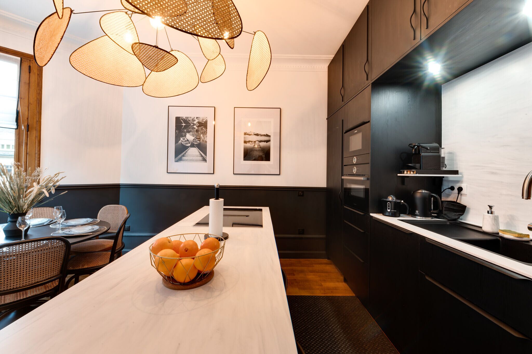 Une cuisine moderne avec des meubles de couleur sombre, un plan de travail blanc et un luminaire suspendu.