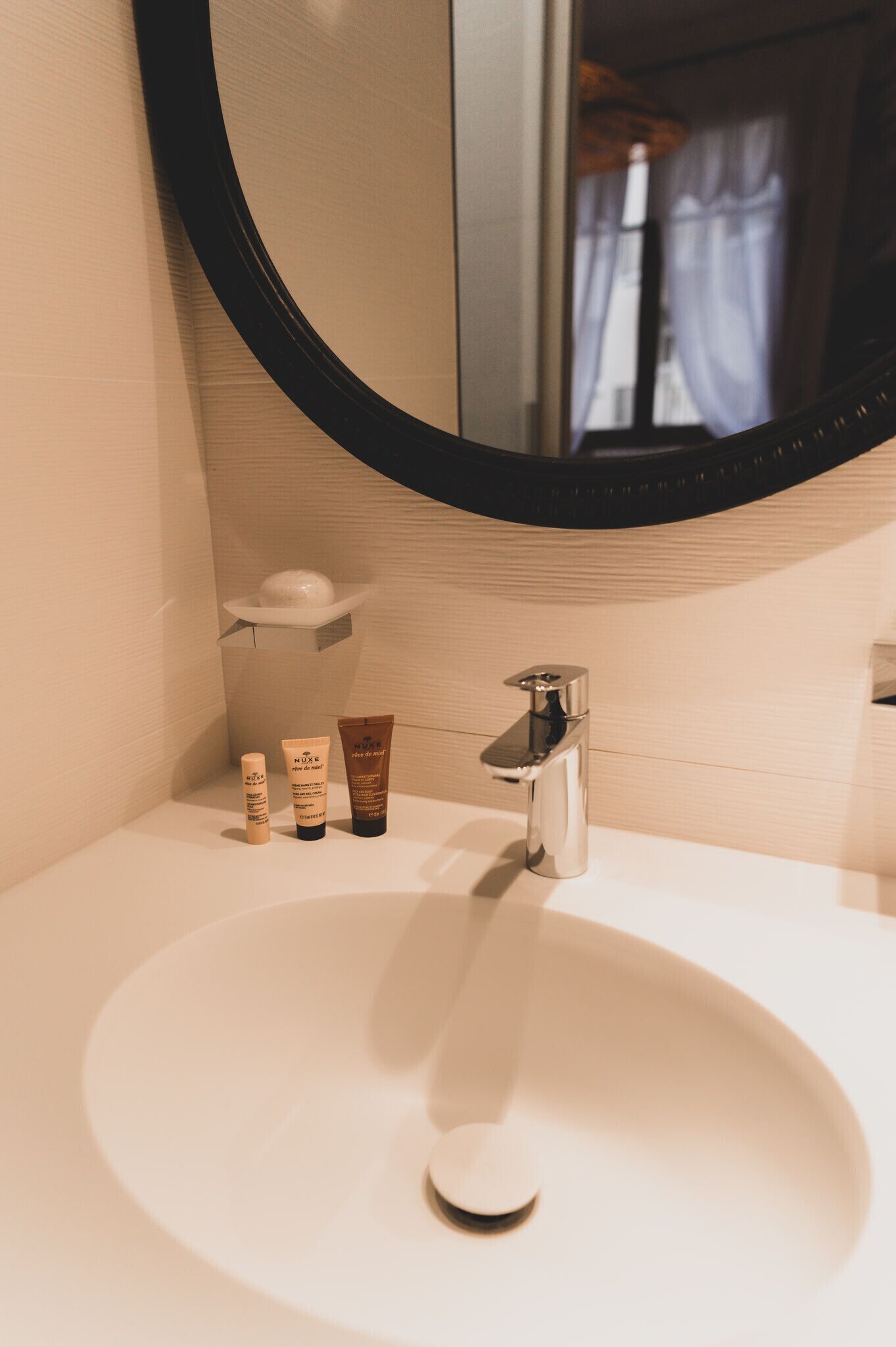 Un baño con lavamanos blanco, un espejo y tres productos para el cuidado de la piel sobre el mostrador.