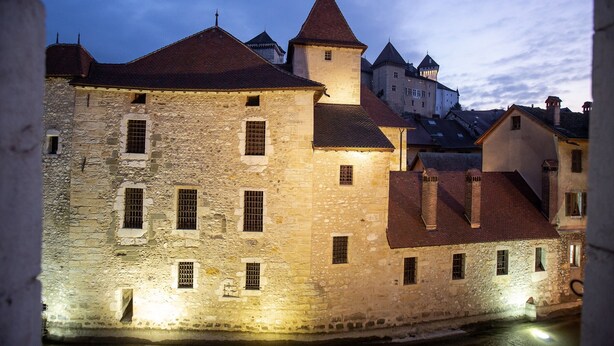 A historic stone building with multiple windows and a tower, likely a hotel or inn, with a river in the foreground. - LaSuitedu12 - Aprtement for 2 people view of the Old Prison (Annecy)