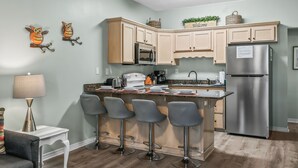 A kitchen with a central island, bar stools, a refrigerator, and decorative wall art. - 3 Bedroom Townhome 87B, one block to beach, close to casinos, & attractions (Gulfport)