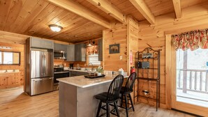 A wooden cabin kitchen with a central island, stainless steel appliances, and a view of the mountains.