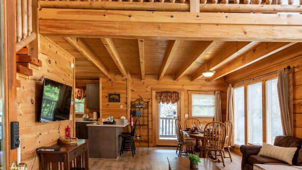 A wooden cabin interior with a dining area, kitchen, and a balcony.